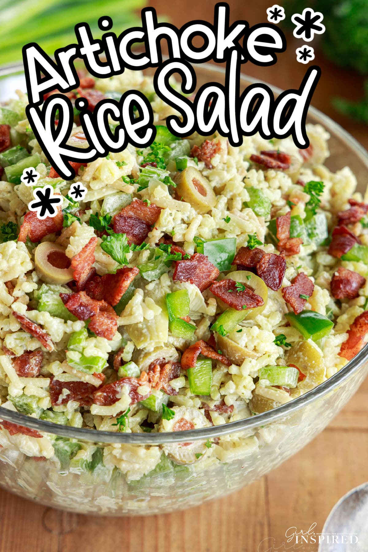 Glass bowl of artichoke rice salad on a wooden board.