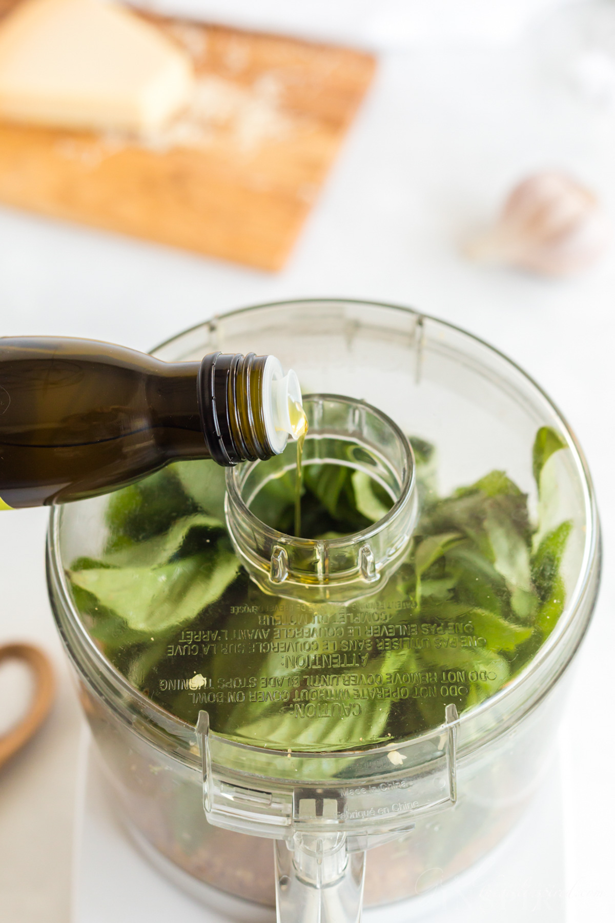 Olive oil drizzled into open cap of food processor as lemon basil pesto is  made.