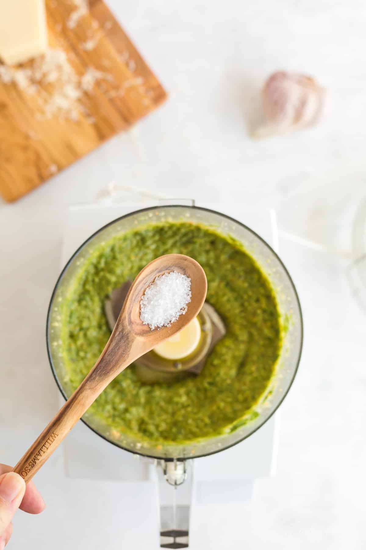 Wooden teaspoon of salt added to lemon basil pesto mixture.