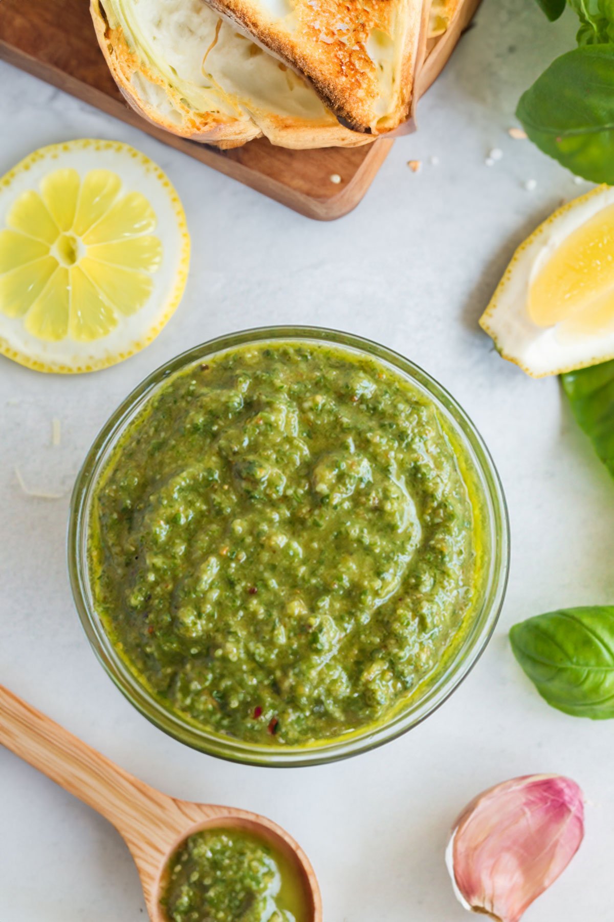 Lemon pesto in glass bowl with crusty bread, lemon slices, basil leaves, and wooden spoon.