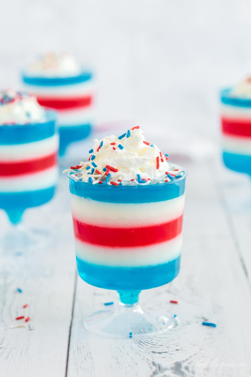 red white and blue jello layered in plastic footed cups with whipped cream and sprinkles