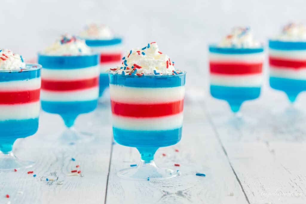 red white and blue jello layered in plastic footed cups with whipped cream and sprinkles