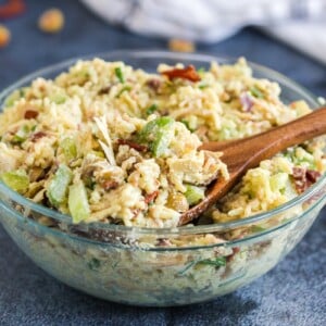 Glass bowl of artichoke rice salad with wooden spoon.