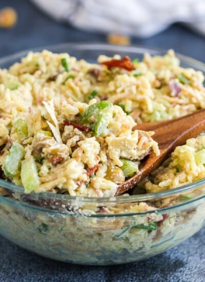Glass bowl of artichoke rice salad with wooden spoon.