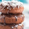 stack of chocolate baked donuts with chocolate frosting and toppings: coconut, sprinkles, and mini chocolate chips, on white plate