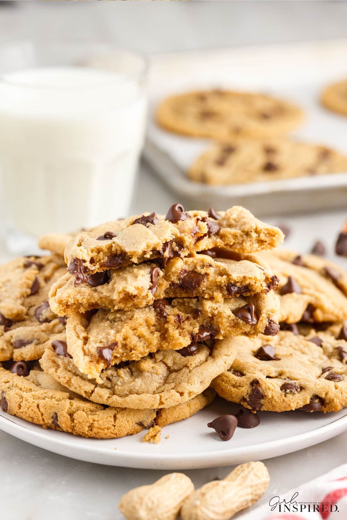 Large peanut butter chocolate chip cookies stacked on a plate with chocolate chips and whole peanuts scattered around.