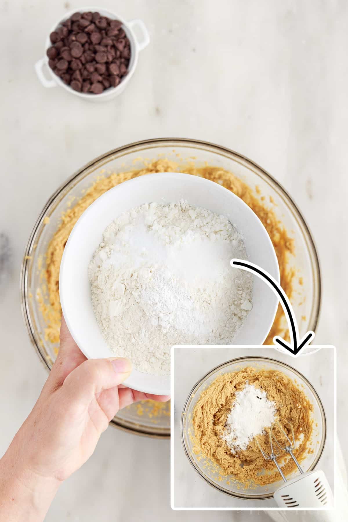 Sifted flour, baking soda, baking powder, and salt, added to the bowl of butter mixture. Small bowl of chocolate chips in the background.