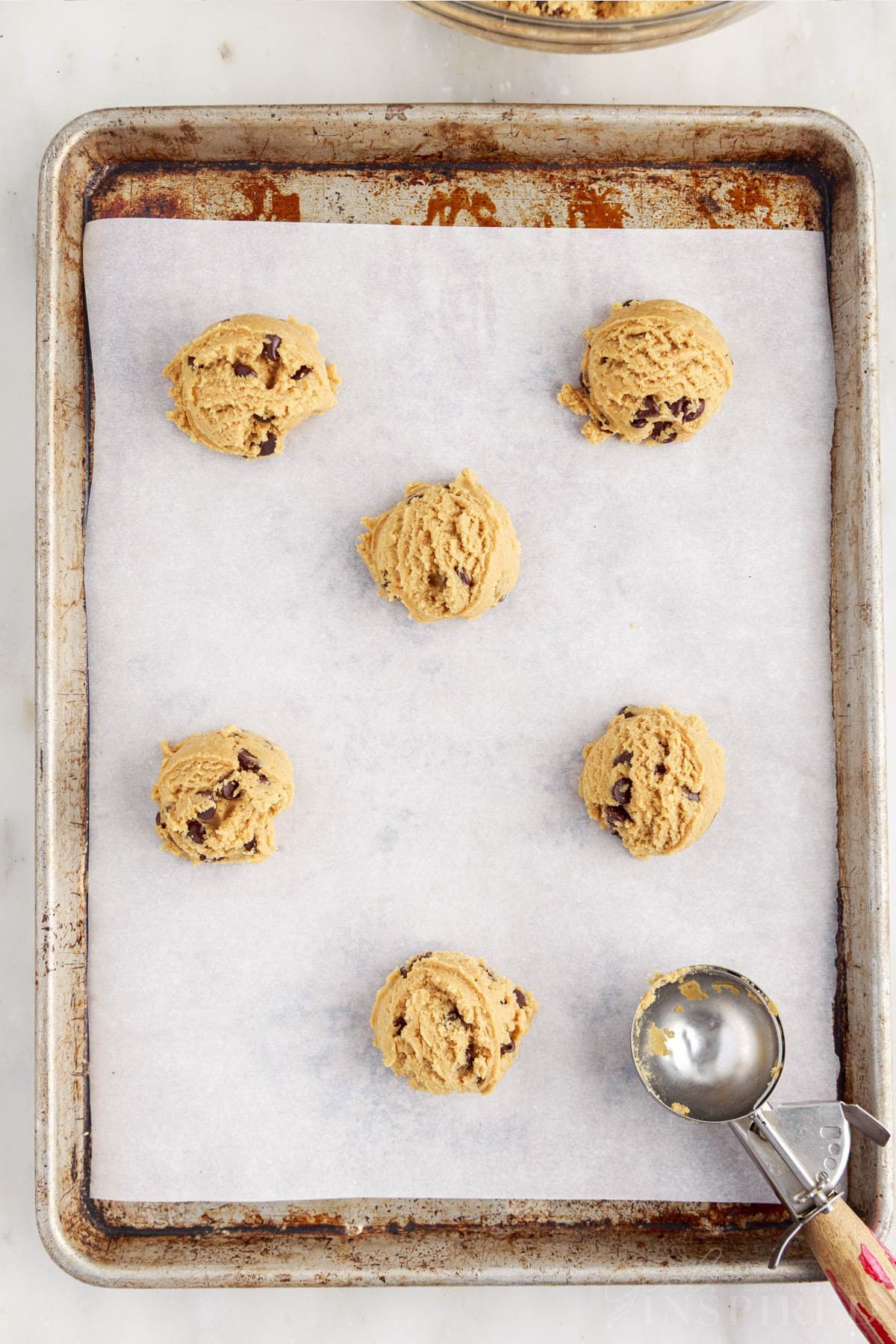 Peanut butter and chocolate chip cookie dough balls added to a parchment-lined baking tray.