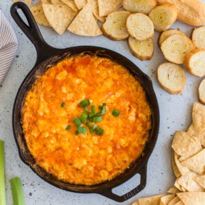 overhead photo of baked buffalo chicken dip with green onions on top, chips and toasted baguette slices, celery sticks