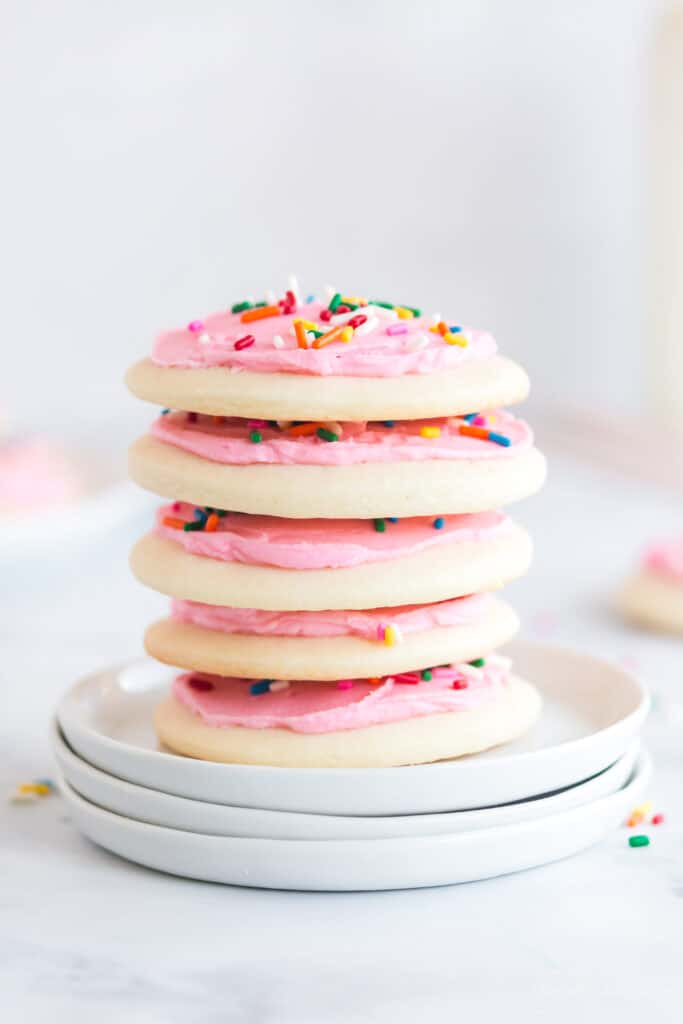 stack of lofthouse cookies with pink frosting and sprinkles on three white plates