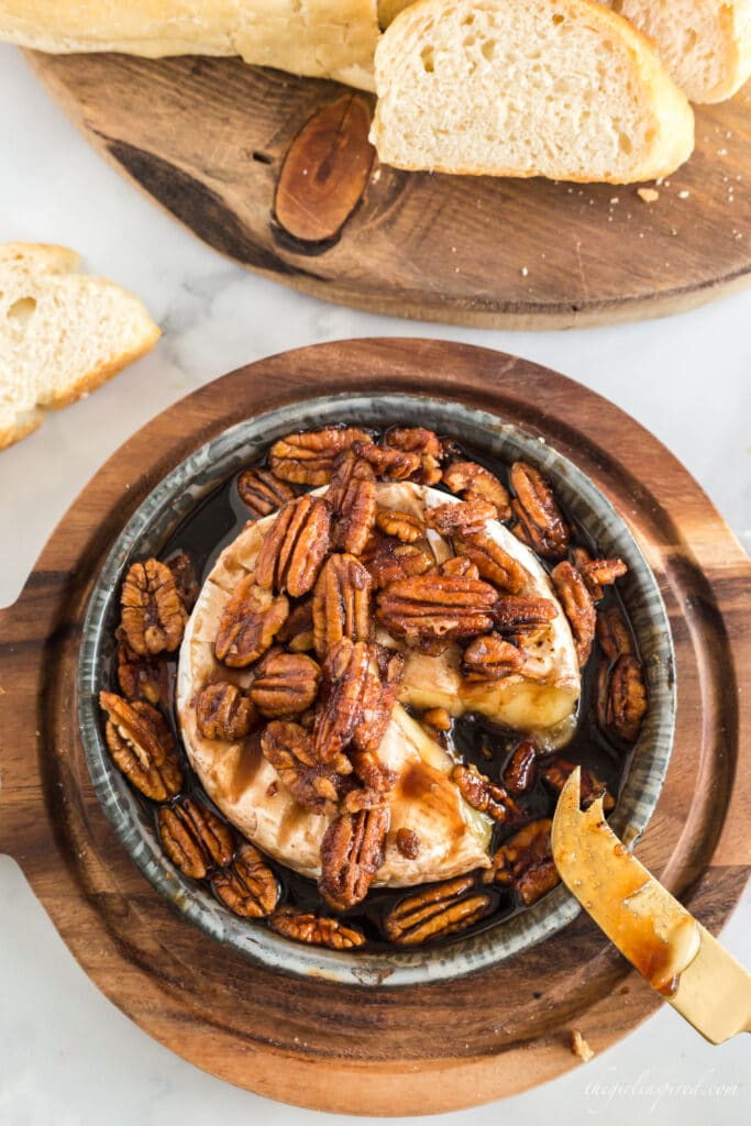 browned pecans and brown sugar over brie in a baking dish on a wooden serving board