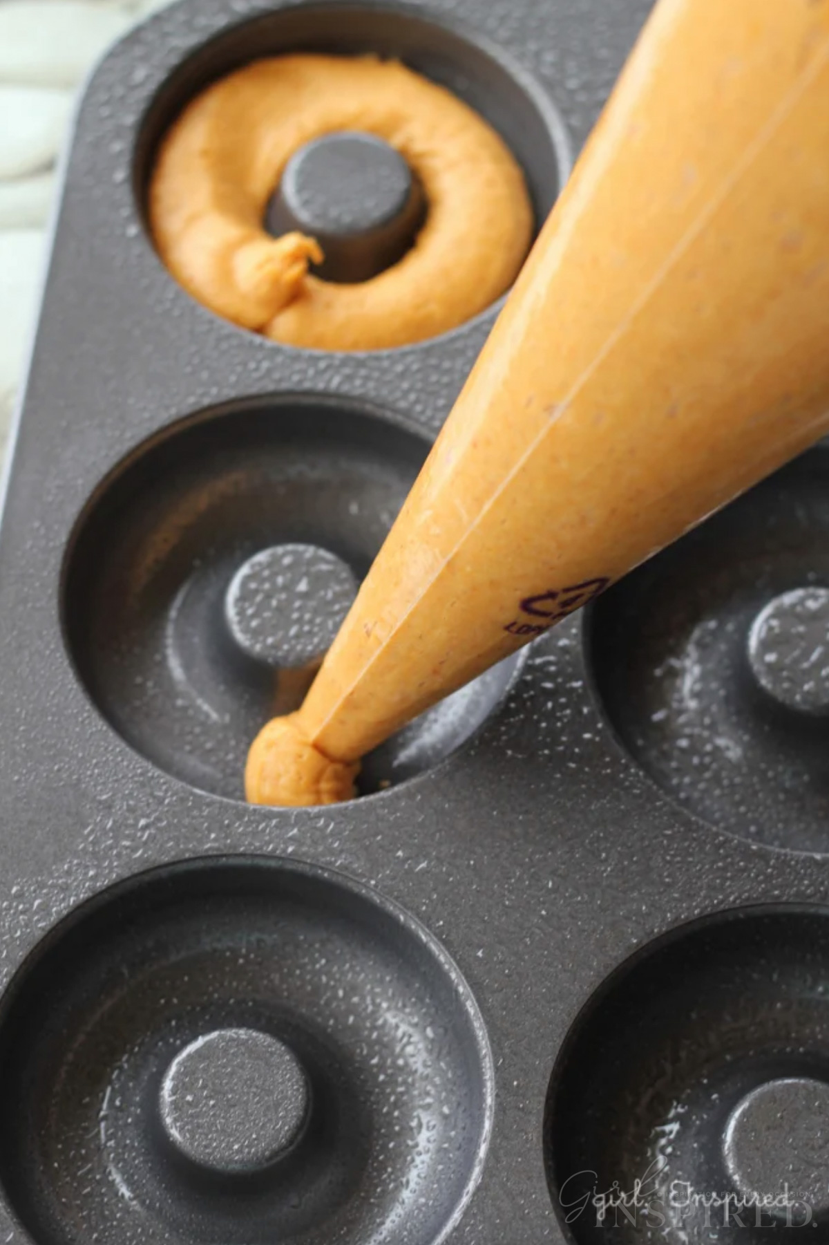 Pastry bag squeezing pumpkin donut batter into donut pan rings.