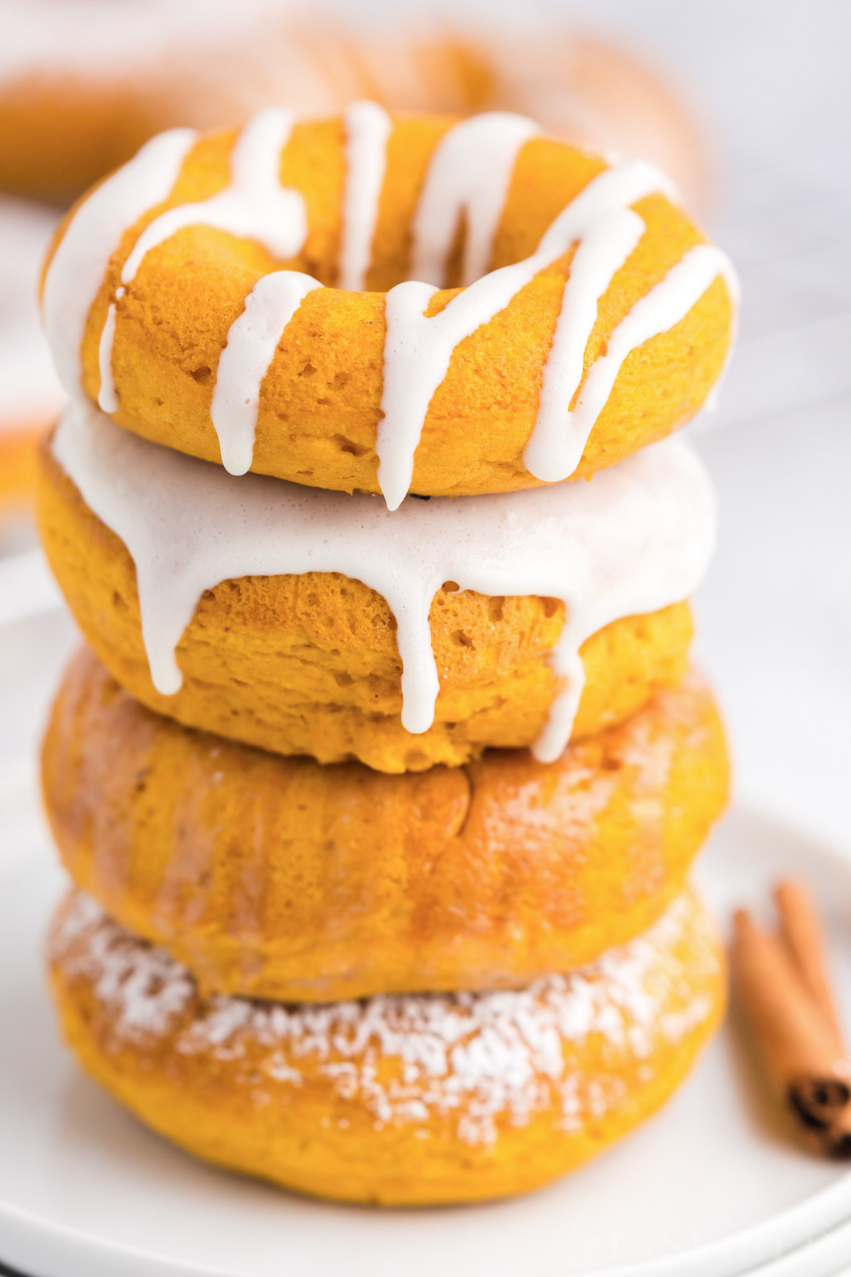 stack of pumpkin donuts with icing or powdered sugar on a small plate with a cinnamon stick.