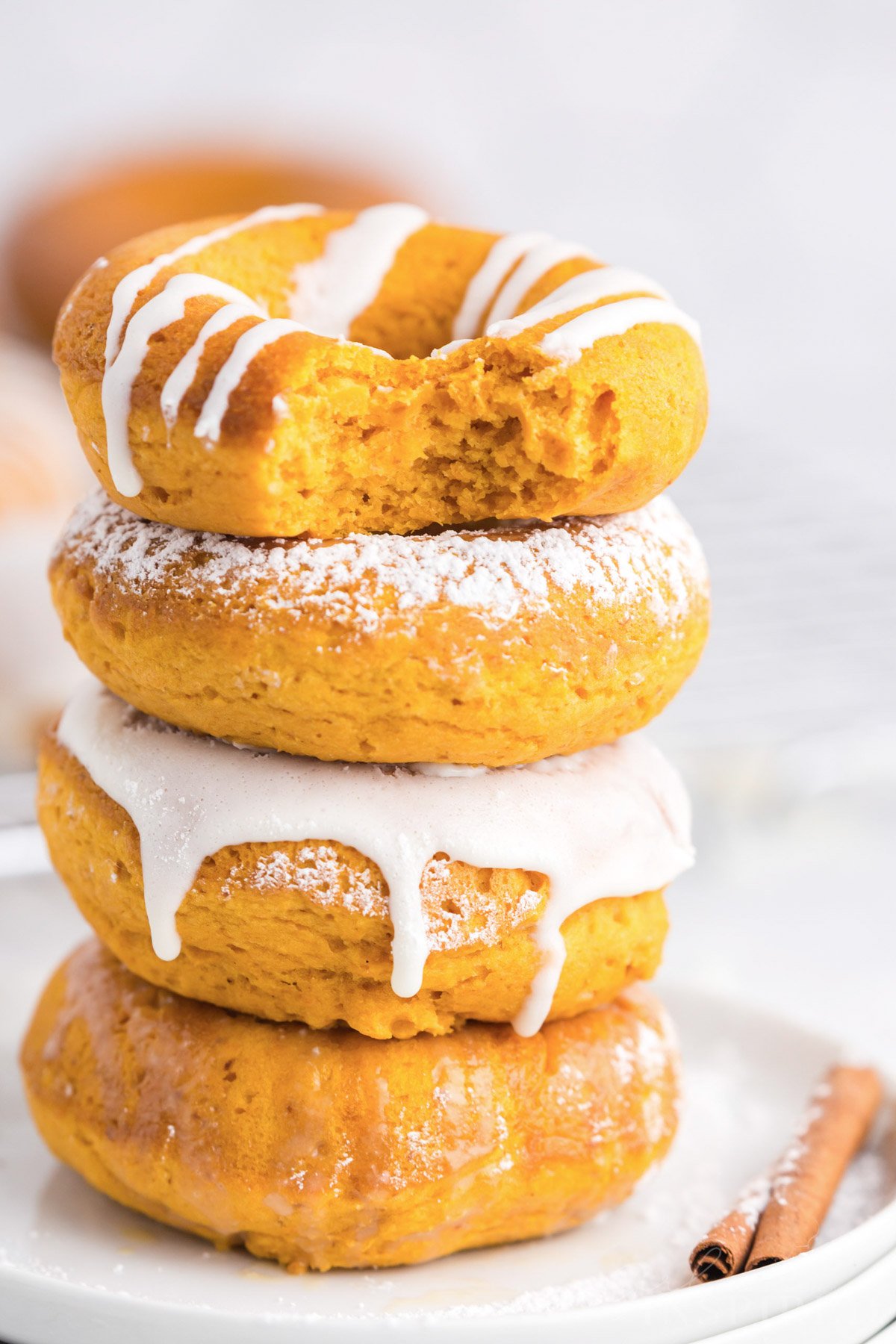 stack of pumpkin donuts with icing or powdered sugar on a small plate with a cinnamon stick.