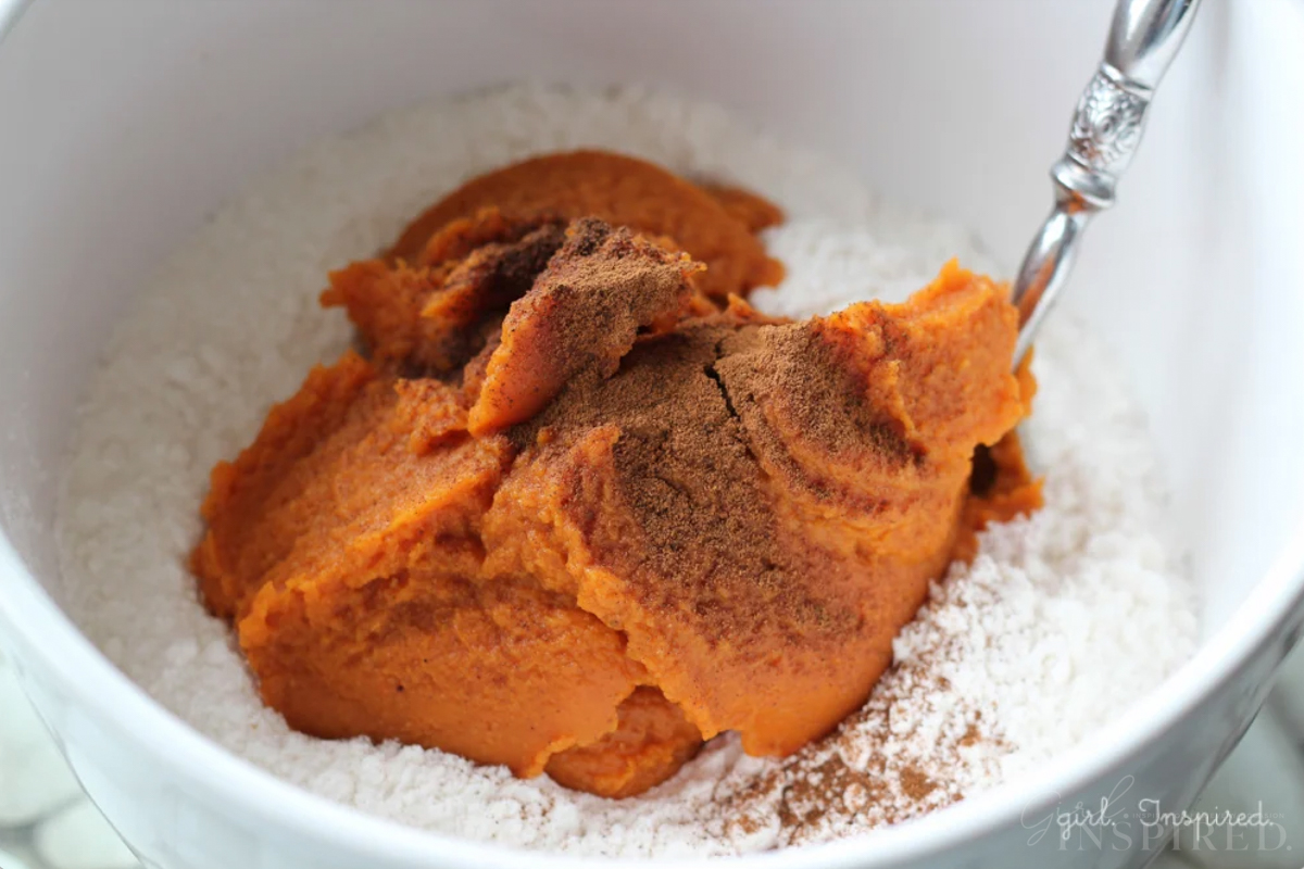 Mixing together pumpkin puree, cake mix, and pumpkin spices in a bowl.