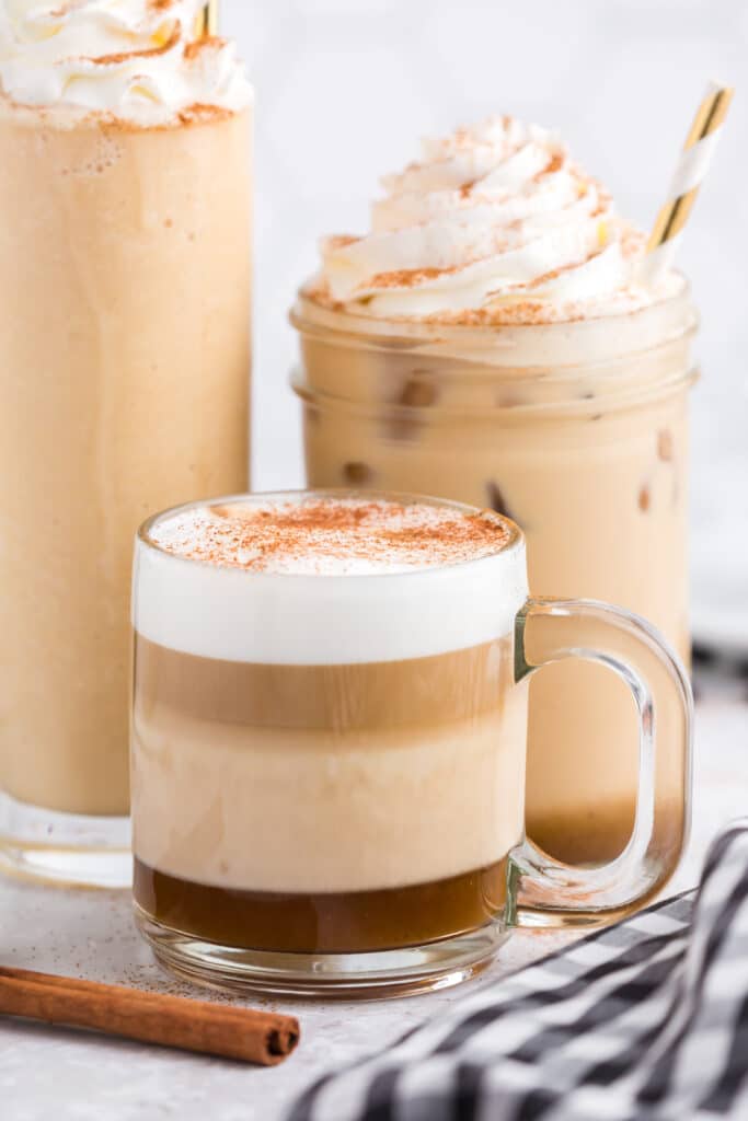 three different sized glasses with pumpkin spice lattes; hot, on ice, and blended, with whipped cream