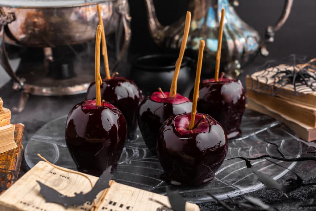 black candy apples on plate with black background and misty bowl and pitcher in background