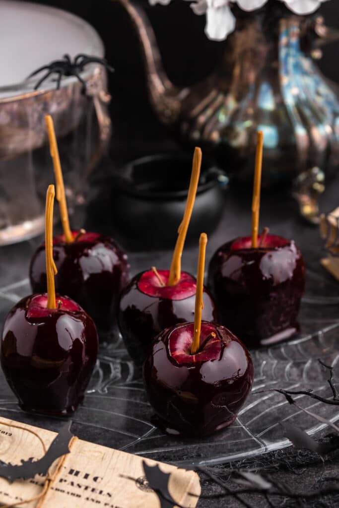 black candy apples on plate with black background and misty bowl and pitcher in background