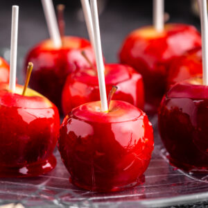 close up of red candy apples on a plate on black backdrop