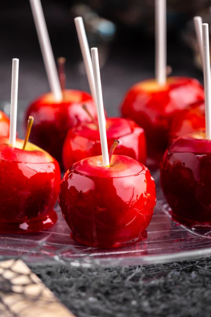 close up of red candy apples on a plate on black backdrop