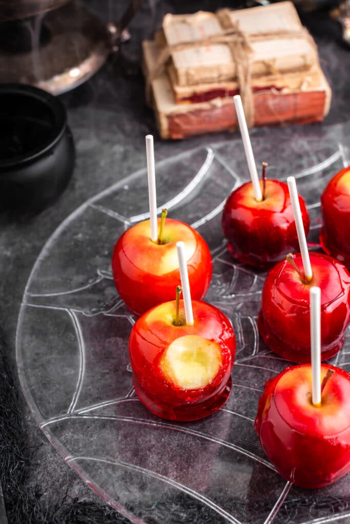 red candy apples on plate with stack of books in background and bite taken from one of the apples