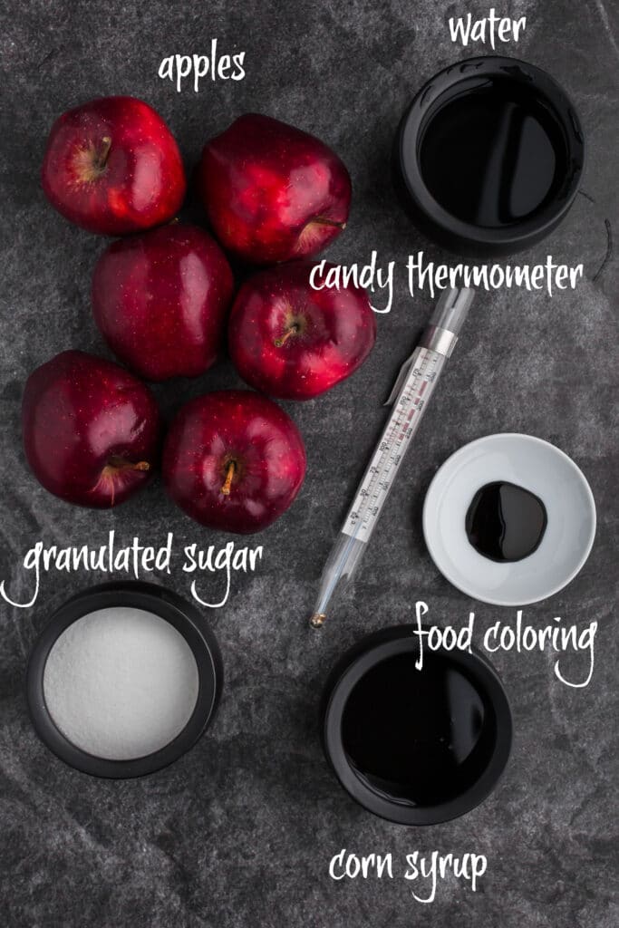 red apples, sugar, corn syrup, and water in black bowls, candy thermometer and black food coloring on white plate - ingredients spread out on black background with text overlay