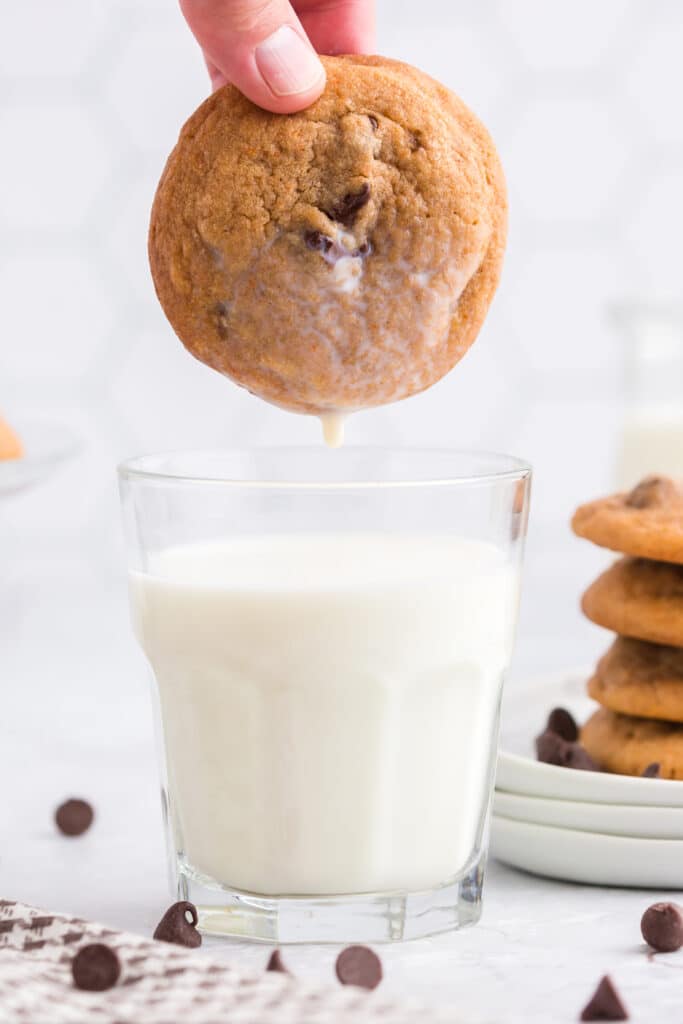 cookie dunked into glass of milk with stack of cookies in the background