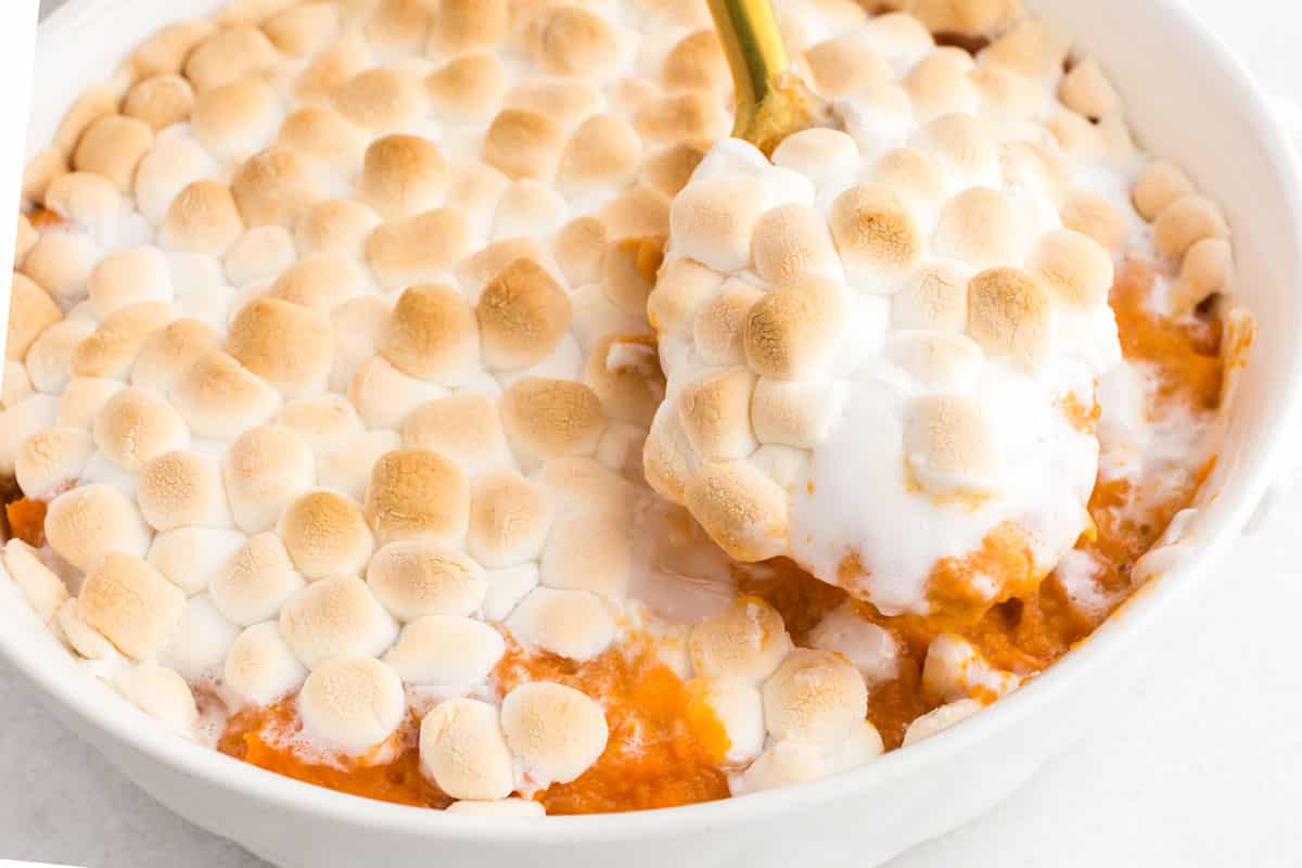 spoon scooping the marshmallow topped candied yams from casserole dish.