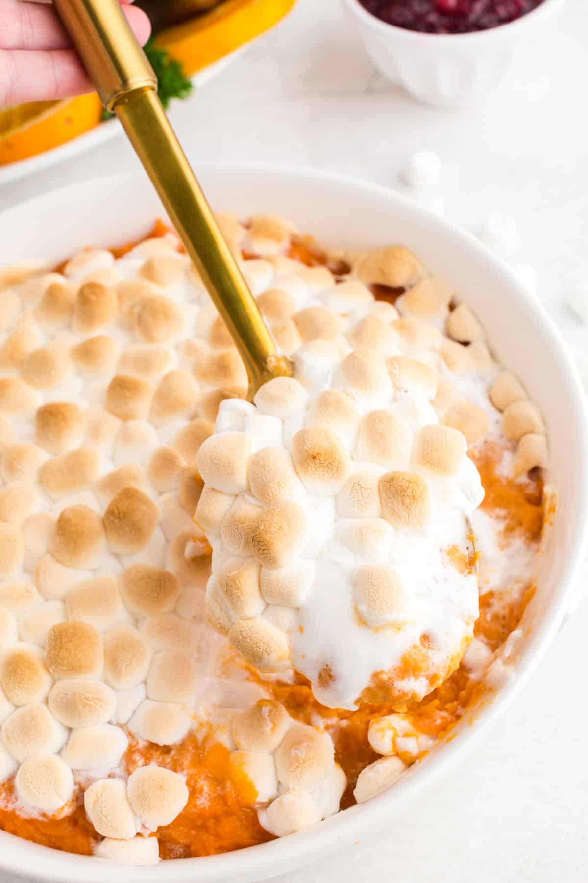 spoon scooping the marshmallow topped candied yams from casserole dish.