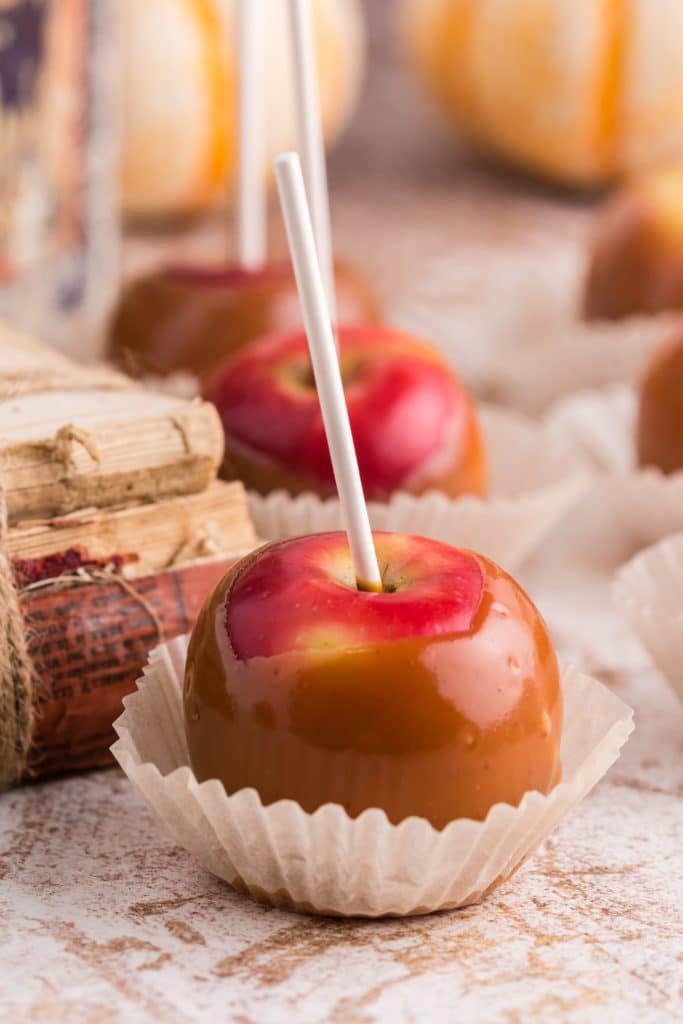 red apples coated in caramel in cupcake wrapper, book stack in background