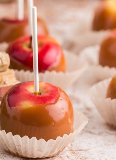 red apples coated in caramel in cupcake wrapper, book stack in background