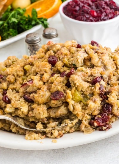 Thanksgiving Stovetop Stuffing on white serving platter with roasted turkey, salt and pepper shakers, and bowl of cranberry sauce in background
