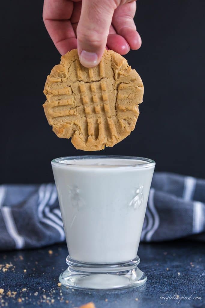 peanut butter cookie held just above glass full of milk