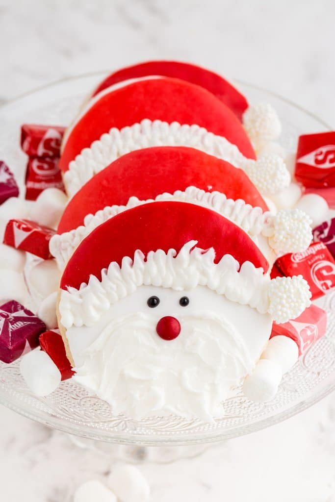 santa claus cookies on glass cake stand with starburst and marshmallows scattered around