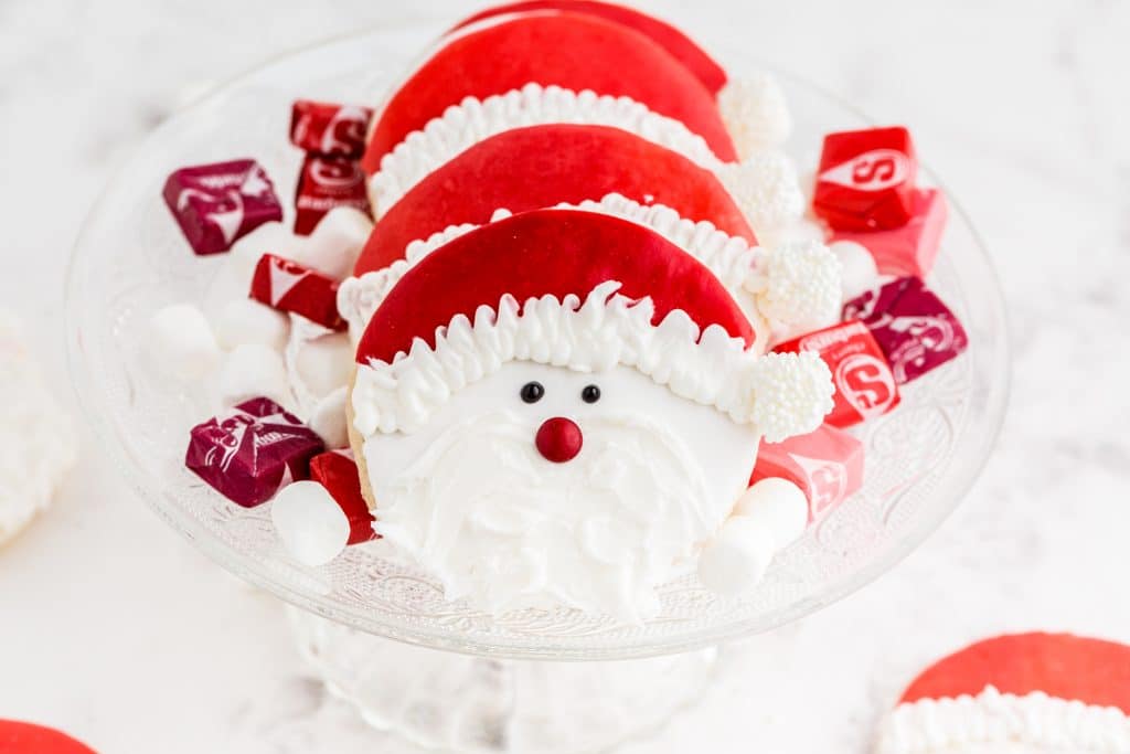 santa cookies on glass cake stand with starburst and marshmallows scattered around