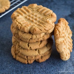 stack of peanut butter cookies with one cookie tilted against the side of stack; cooling rack with cookies in background