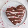 two stacked heart shapes covered in chocolate with white chocolate drizzle and heart sprinkles on white plate