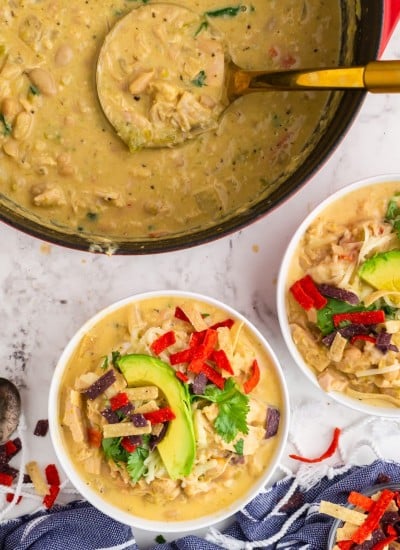 green chili chicken soup in white bowls and red dutch oven, topped with avocado slices and colorful tortilla strips