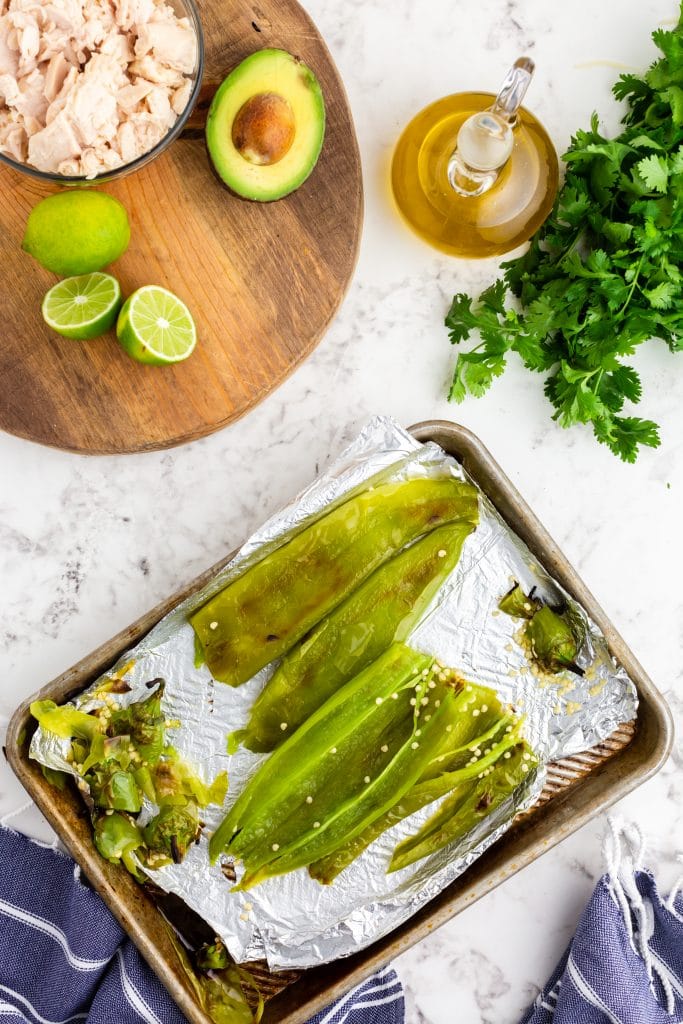 roasted chiles on sheet pan with stems and seeds removed; avocado, lime, chicken and cilantro set nearby