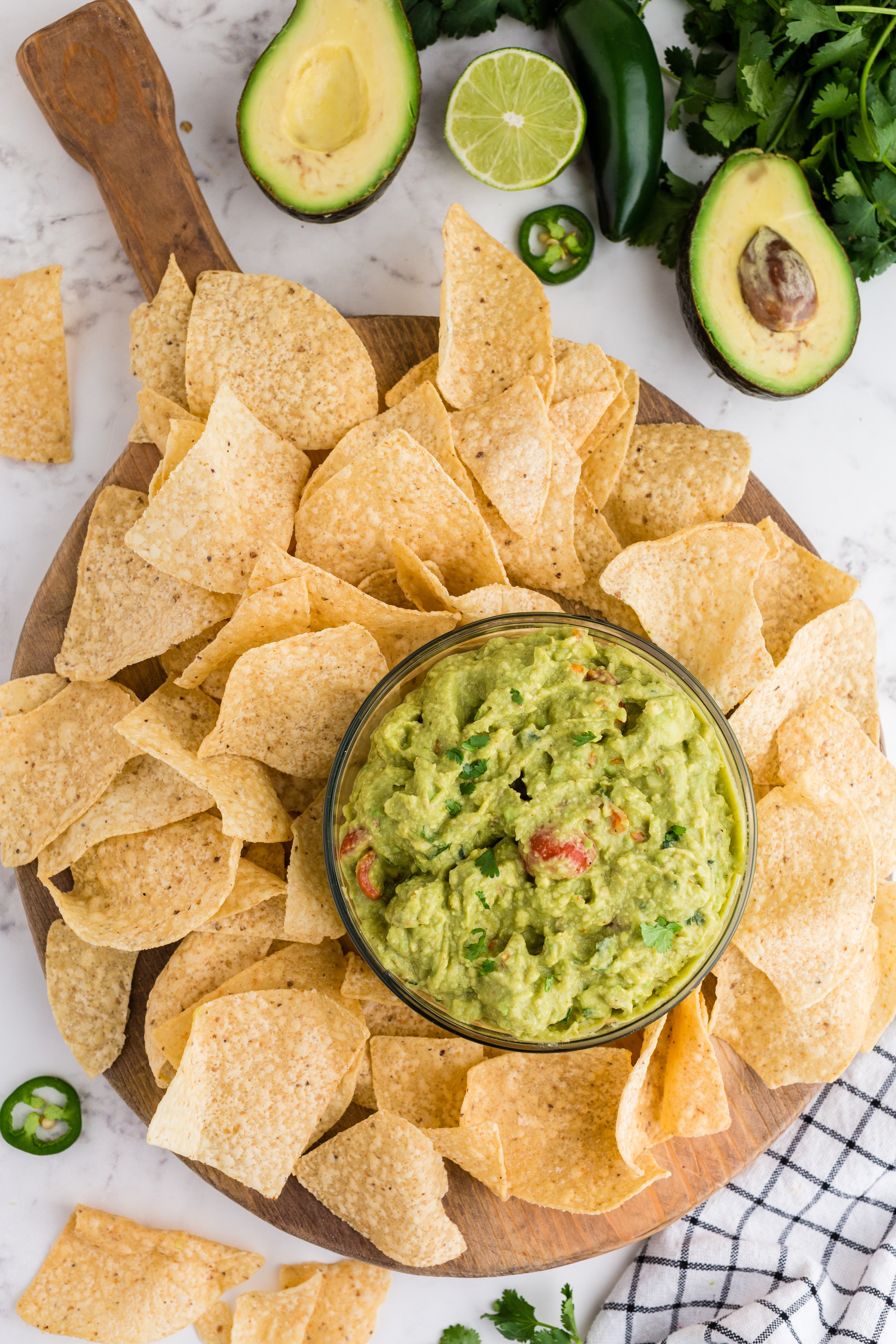 guacamole in clear glass bowl and chips, avocados, and cilantro around