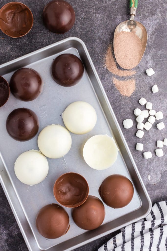dark, white, and milk chocolate half spheres laid out on baking sheet, cocoa in a scoop, mini marshmallows spread out