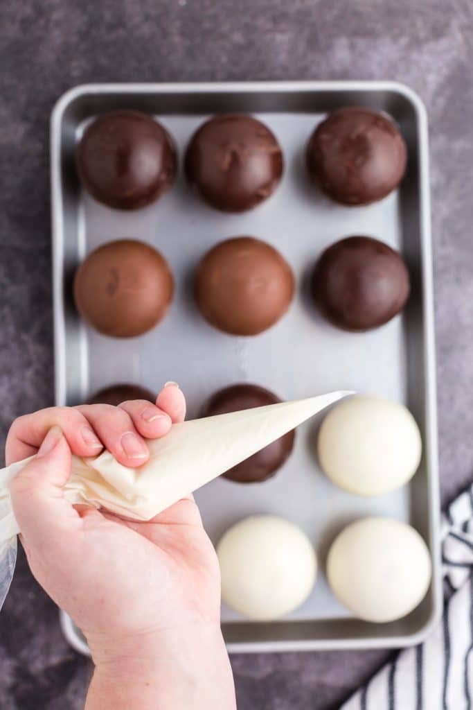 melted white chocolate in a piping bag held over tray of finished hot chocolate bombs