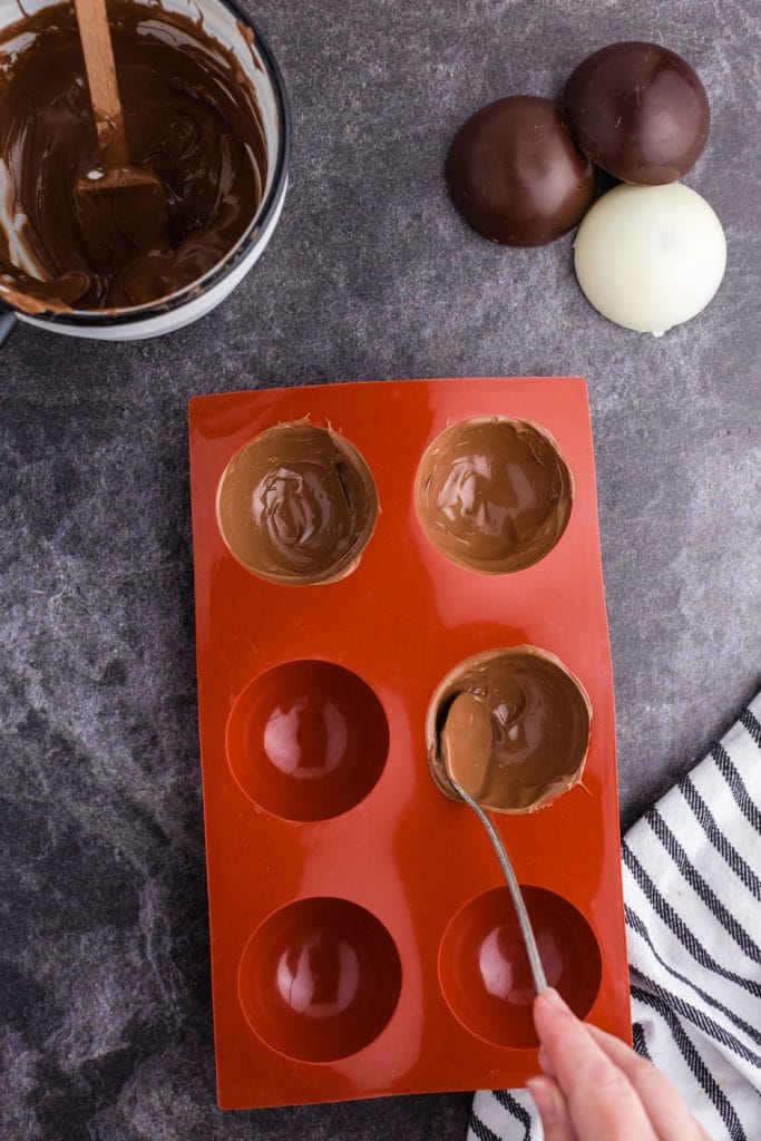 spoon coating melted chocolate in sphere mold