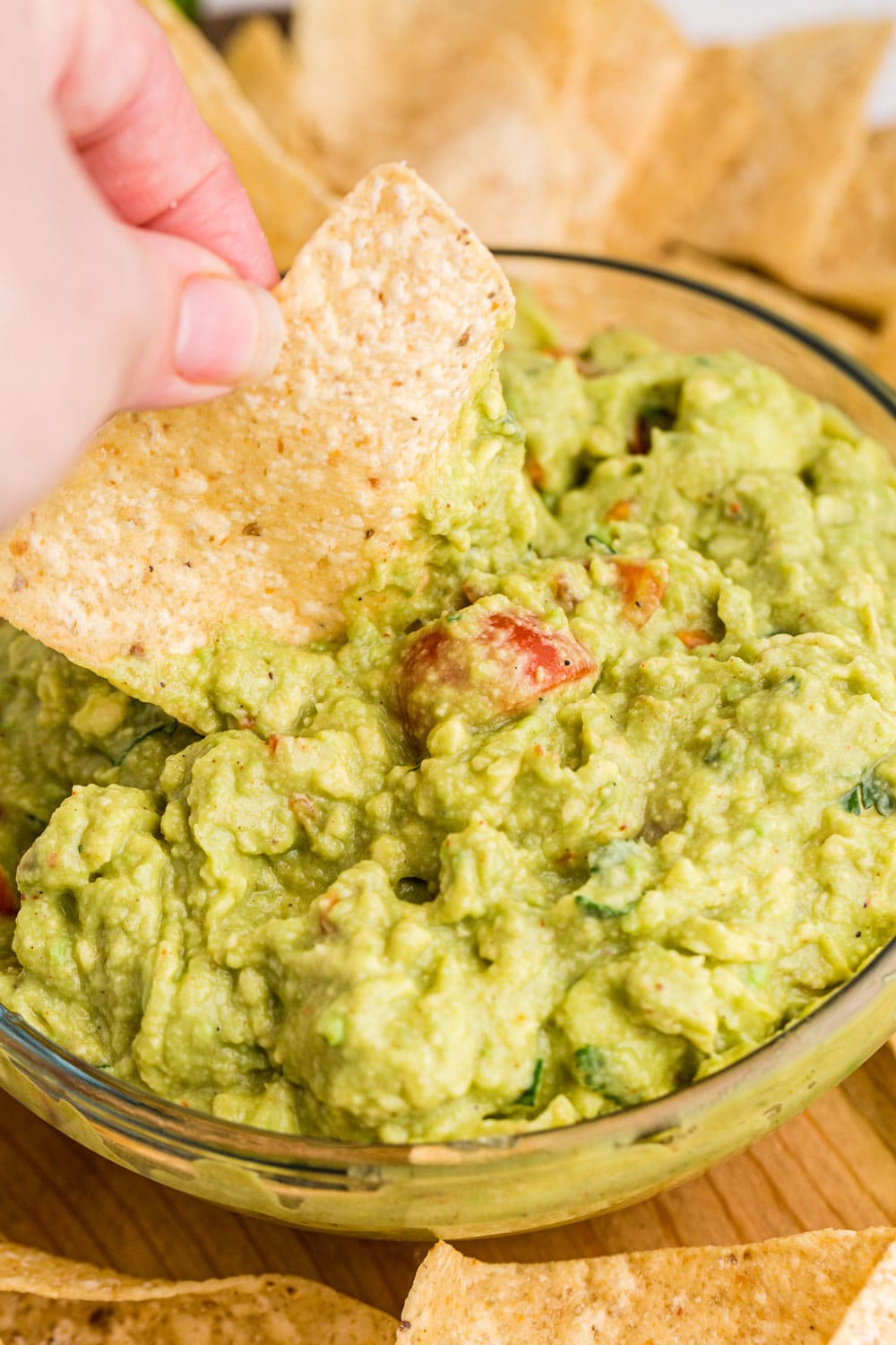 guacamole in clear glass bowl with chip dipping into it and chips around