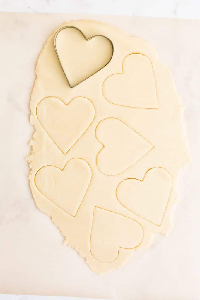 cookie dough rolled out on parchment paper with heart shapes cut into it