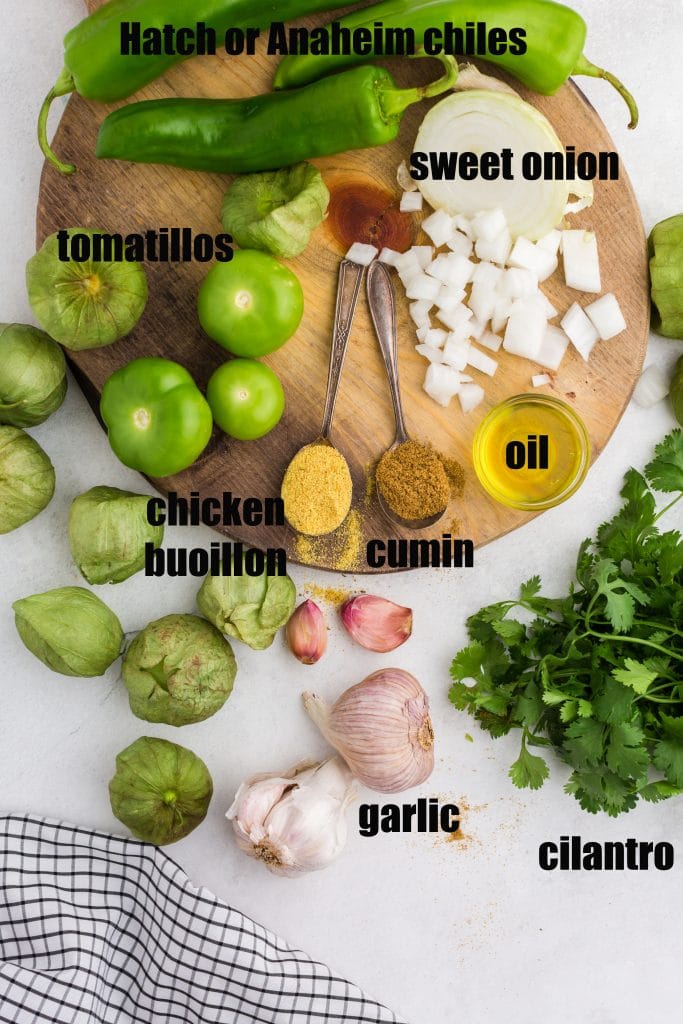 Ingredients for green enchilada sauce laid out on counter - tomatillos, garlic, cumin, bouillon, onion, oil, and fresh cilantro