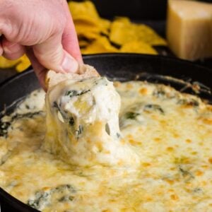 Chip with a scoop of spinach artichoke dip (without mayo) held over skillet full of dip.