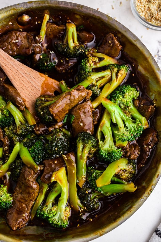 beef and broccoli in saute pan with wooden spoon