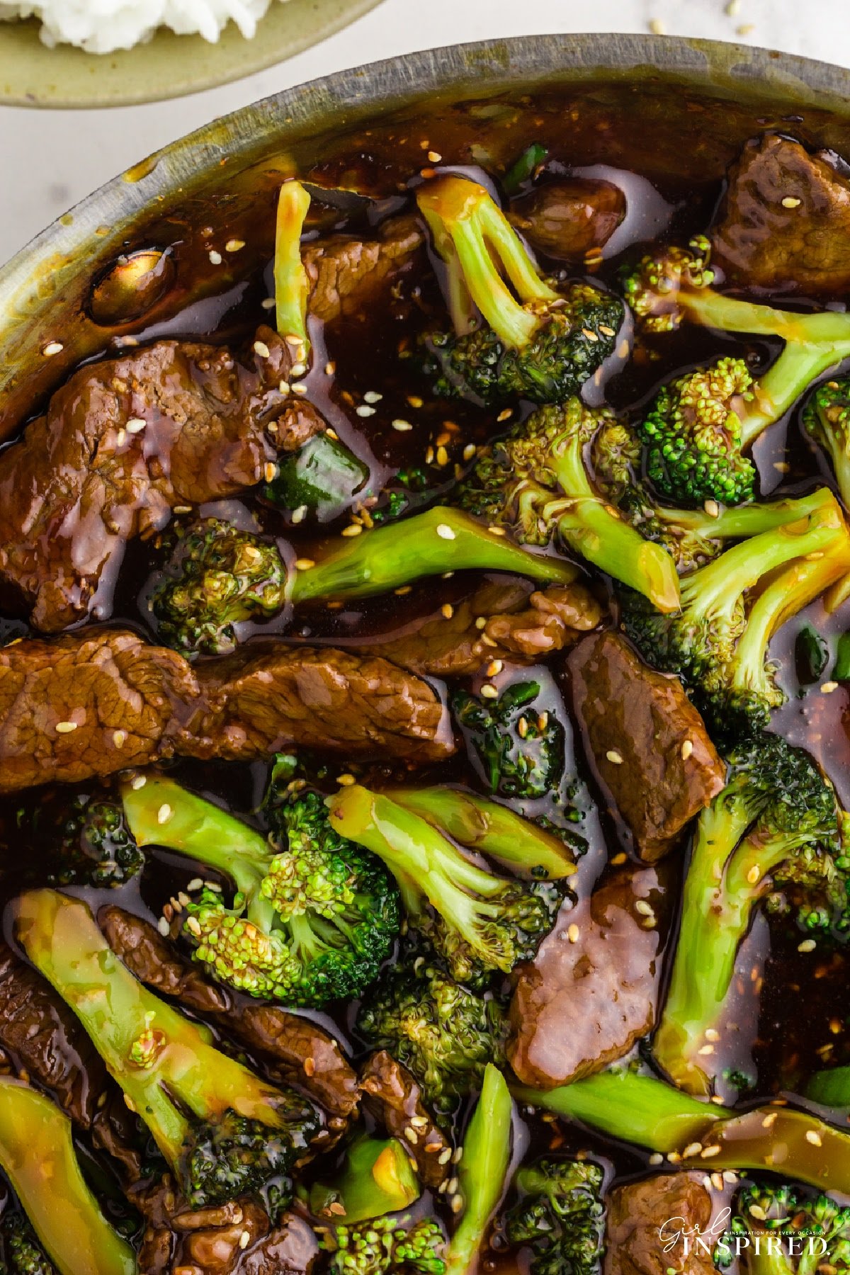 Closeup of strips of beef and broccoli florets in thick sauce with sesame seeds.