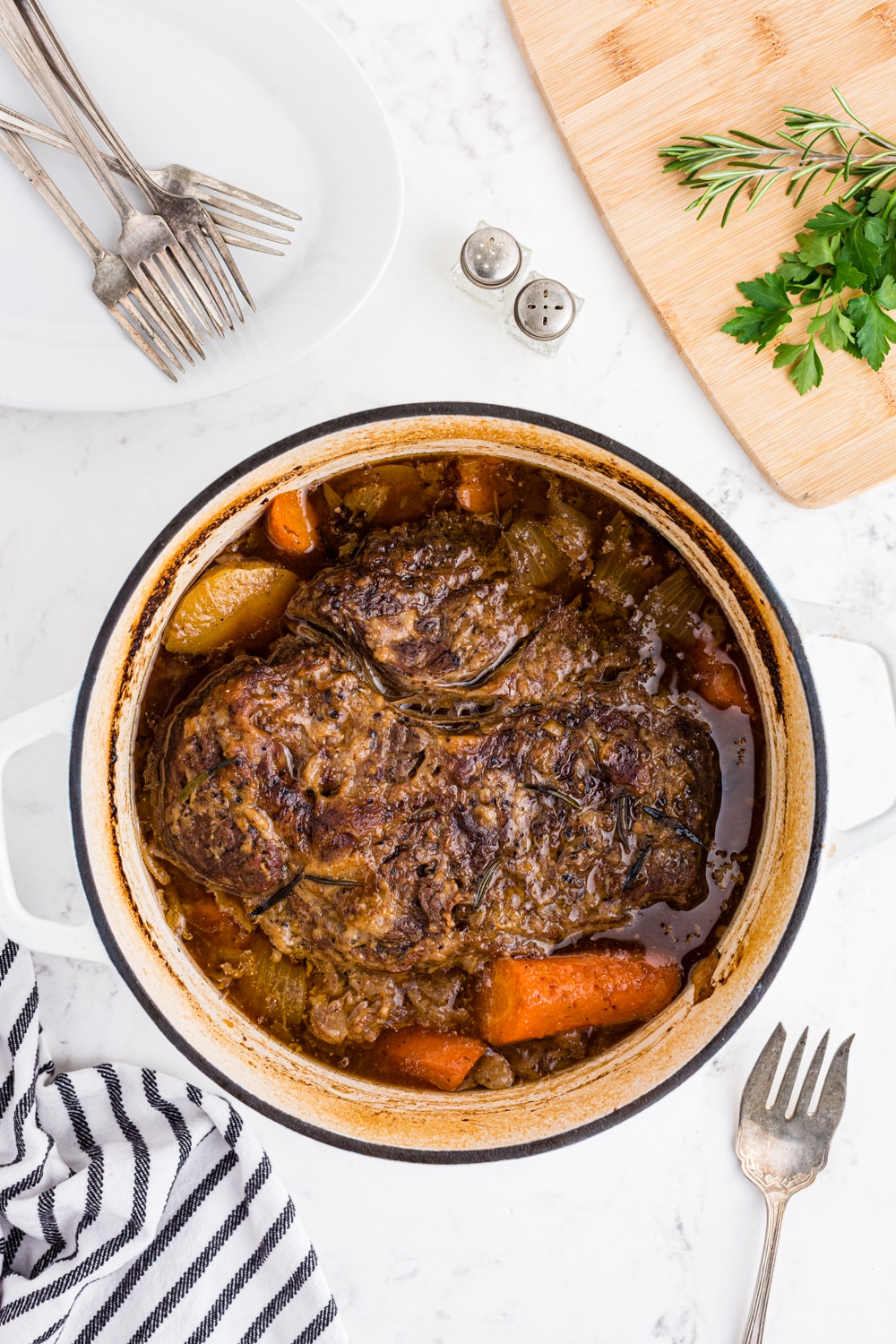 cooked roast with carrots and potatoes in a Dutch oven with serving dishes around